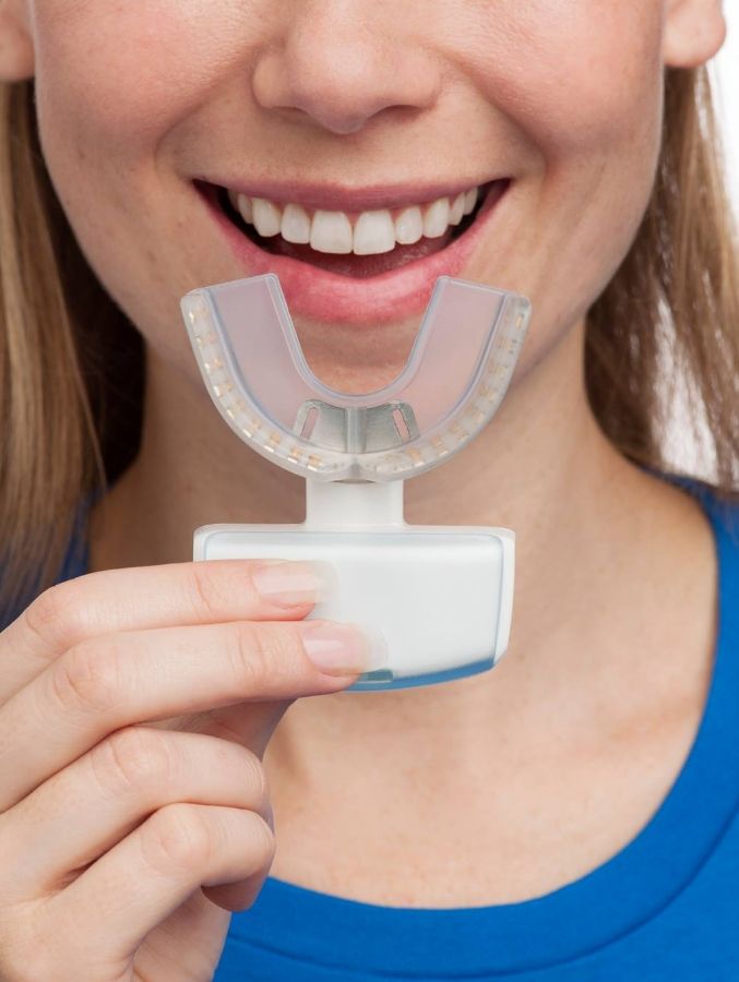 Smiling woman holding aligner shaped device for OrthoPulse in Cary
