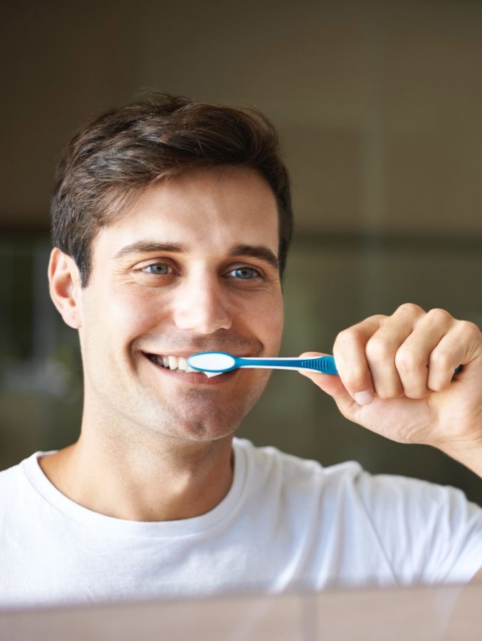 Man smiling while brushing his teeth