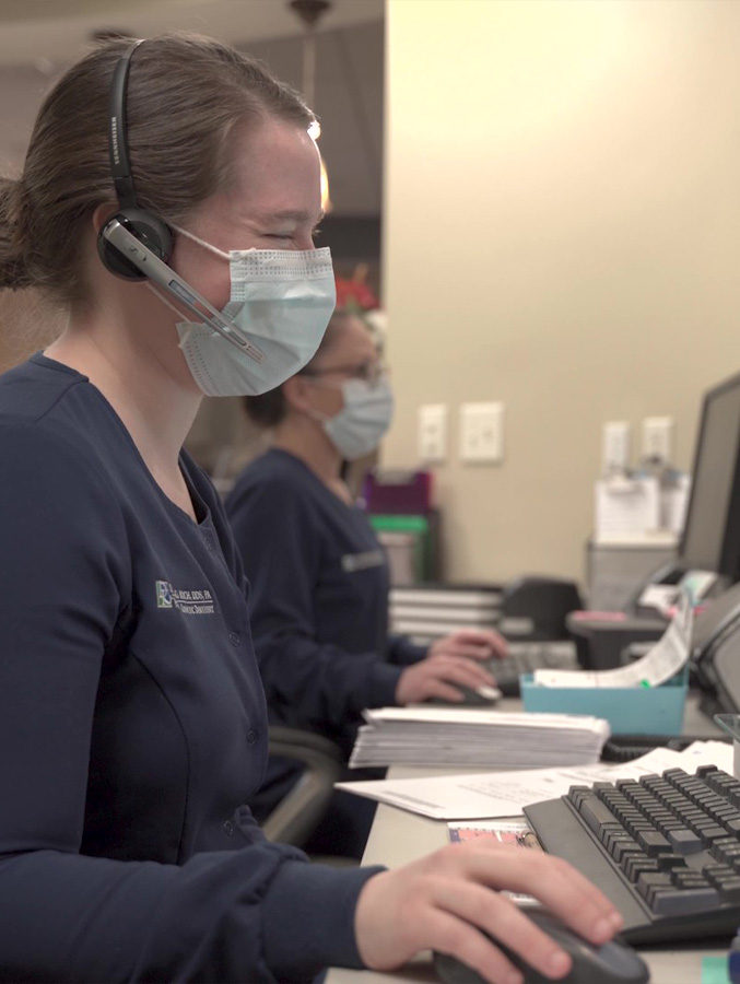 Smiling dental team member wearing face mask at front desk
