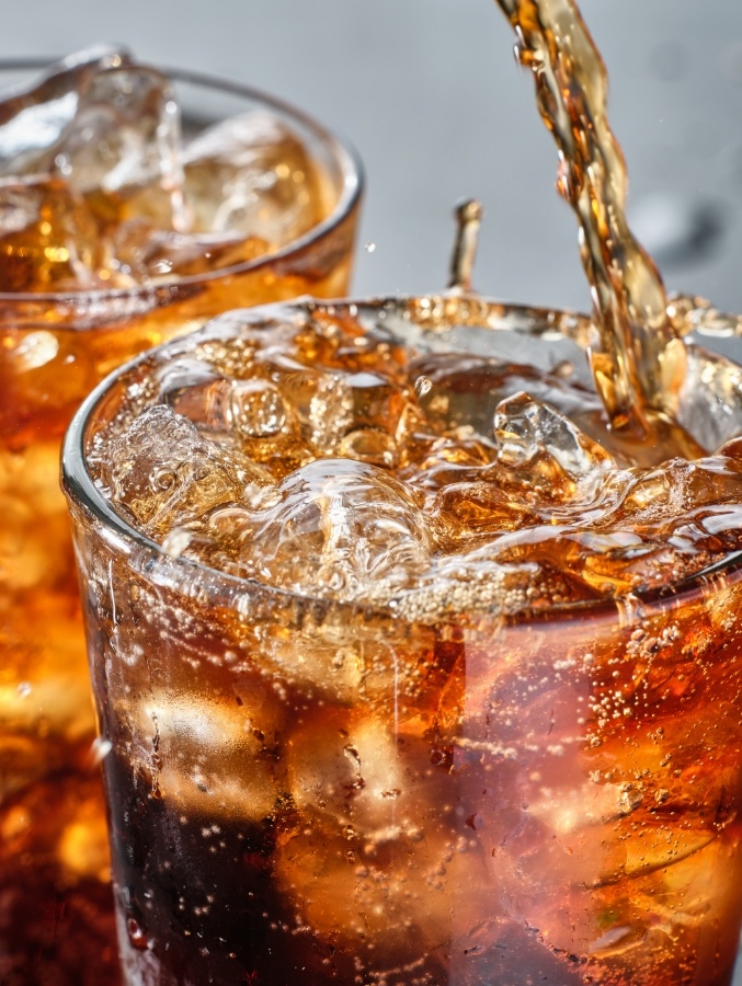 Brown soda being poured into a glass with ice