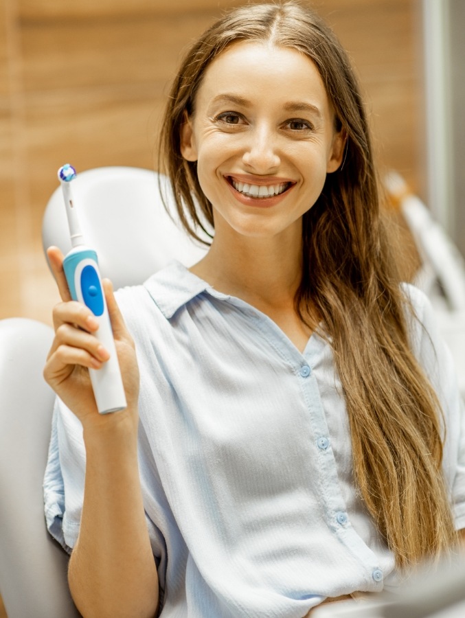 Smiling woman in dental chair holding electric toothbrush