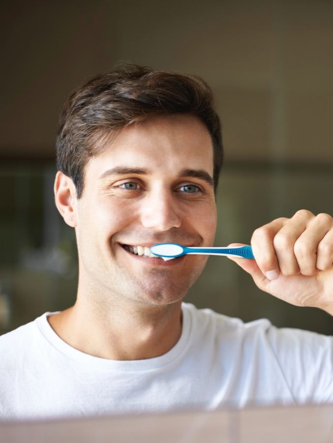 Man smiling while brushing his teeth