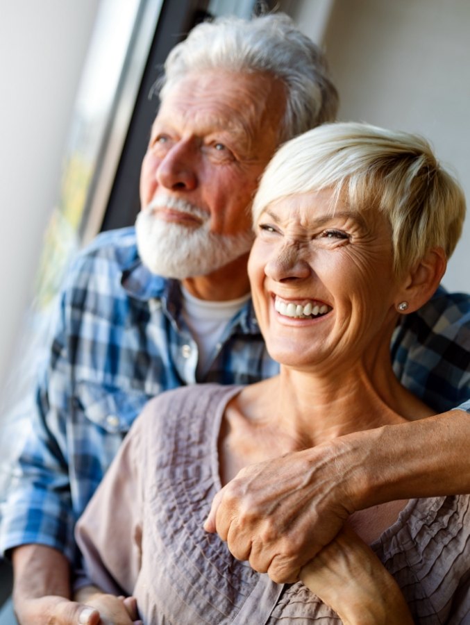 Senior man and woman with fixed hybrid dental prosthetics in Cary looking out window together