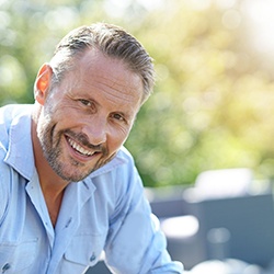 Man in light blue shirt sitting outside and smiling