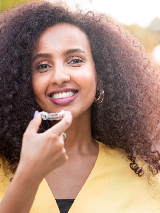 Smiling woman holding clear aligner for Invisalign in Cary