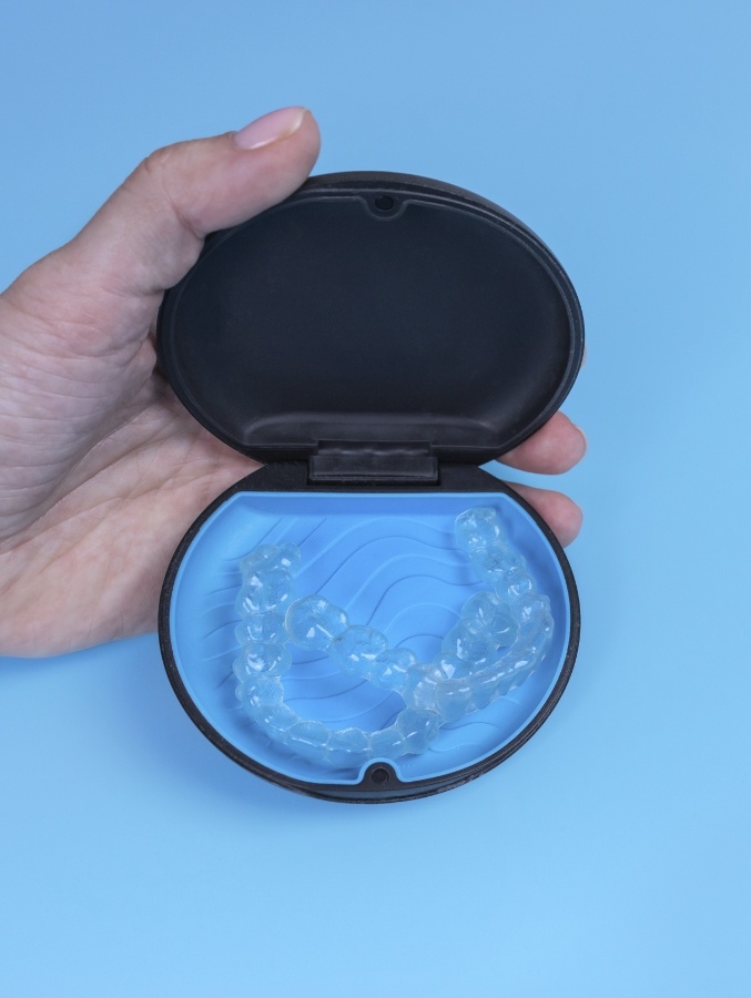 Hand holding Invisalign case with two clear aligners inside of it