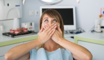 Woman in dental chair covering her mouth in fear