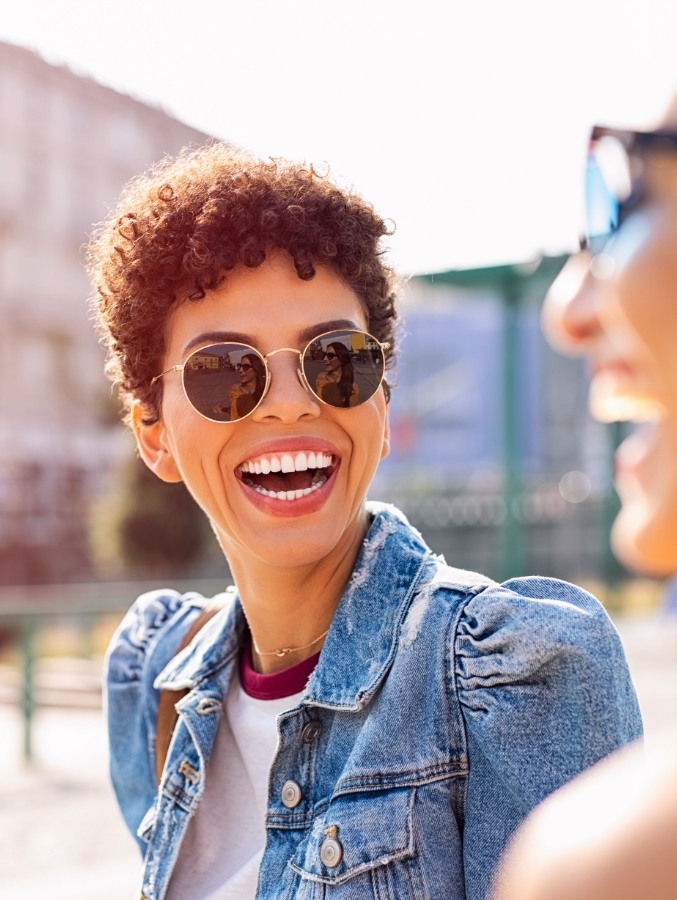 Person in denim shirt laughing outdoors after teeth whitening in Cary