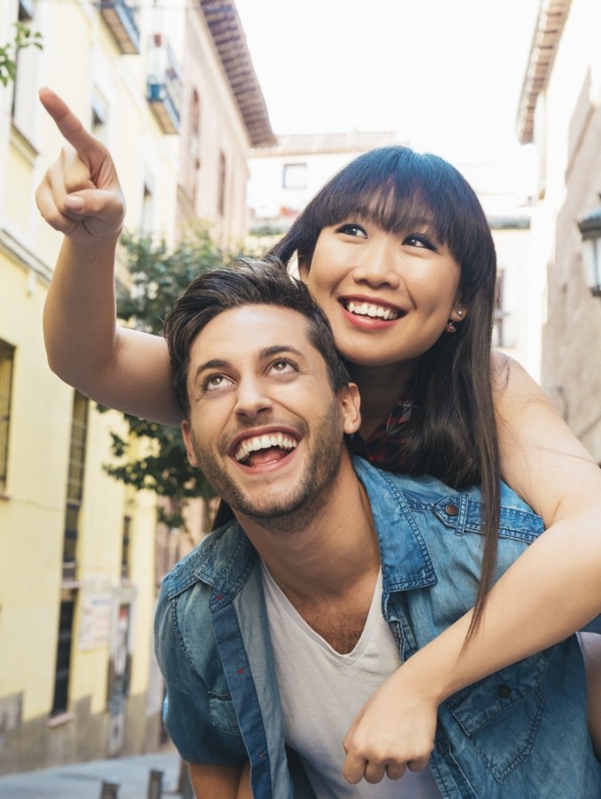 Smiling woman pointing into the distance while hugging smiling man from behind