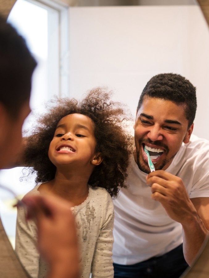 Father and young daughter brushing their teeth together