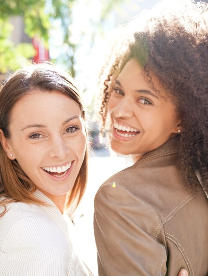 Two women grinning outdoors on sunny day