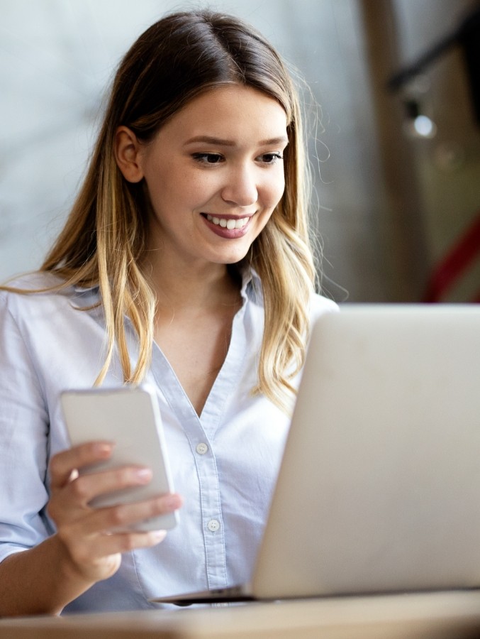 Woman holding laptop and phone during virtual dental consultation in Cary