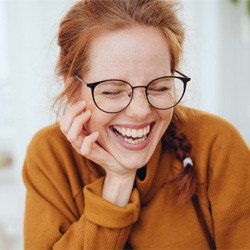 Woman with orange sweater and glasses laughing