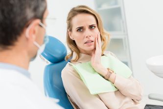 Woman in dental chair touching her cheek