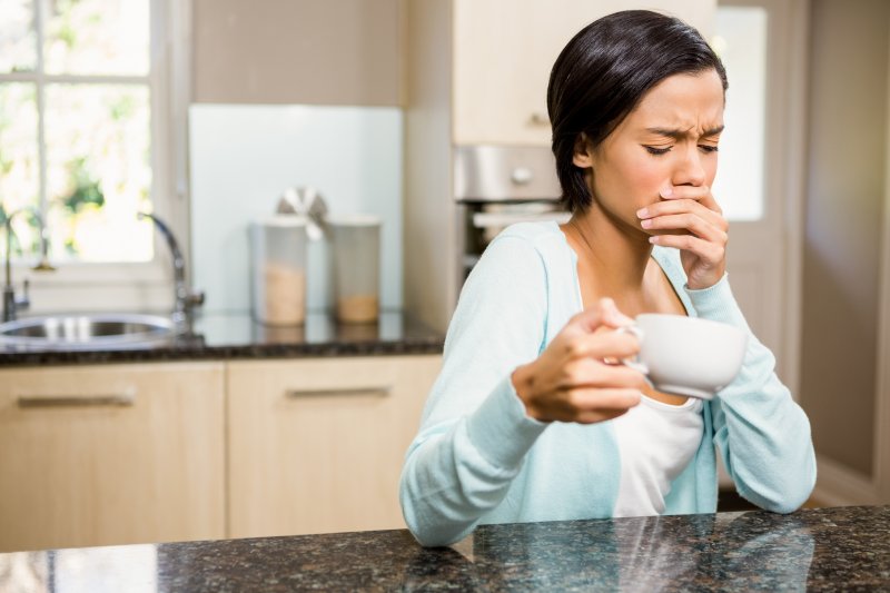 a young woman holding a cup of coffee and covering her mouth because of pain radiating from tooth sensitivity