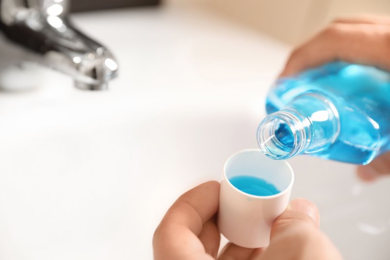 a person pouring mouthwash into a cup in preparation for rinsing 