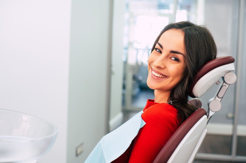 a young woman wearing a red blouse and smiling while waiting for her dentist to arrive