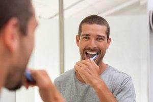 man looking in the mirror brushing his veneers