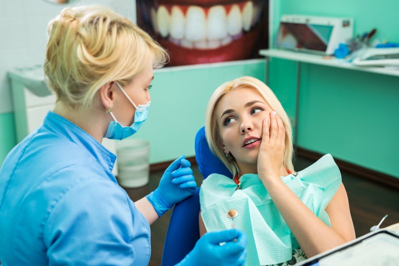 Woman visiting emergency dentist rubbing jaw