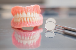 Full dentures next to a mouth mirror for dental checkups