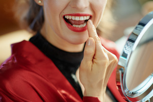 Woman in red jacket checking smile in the mirror